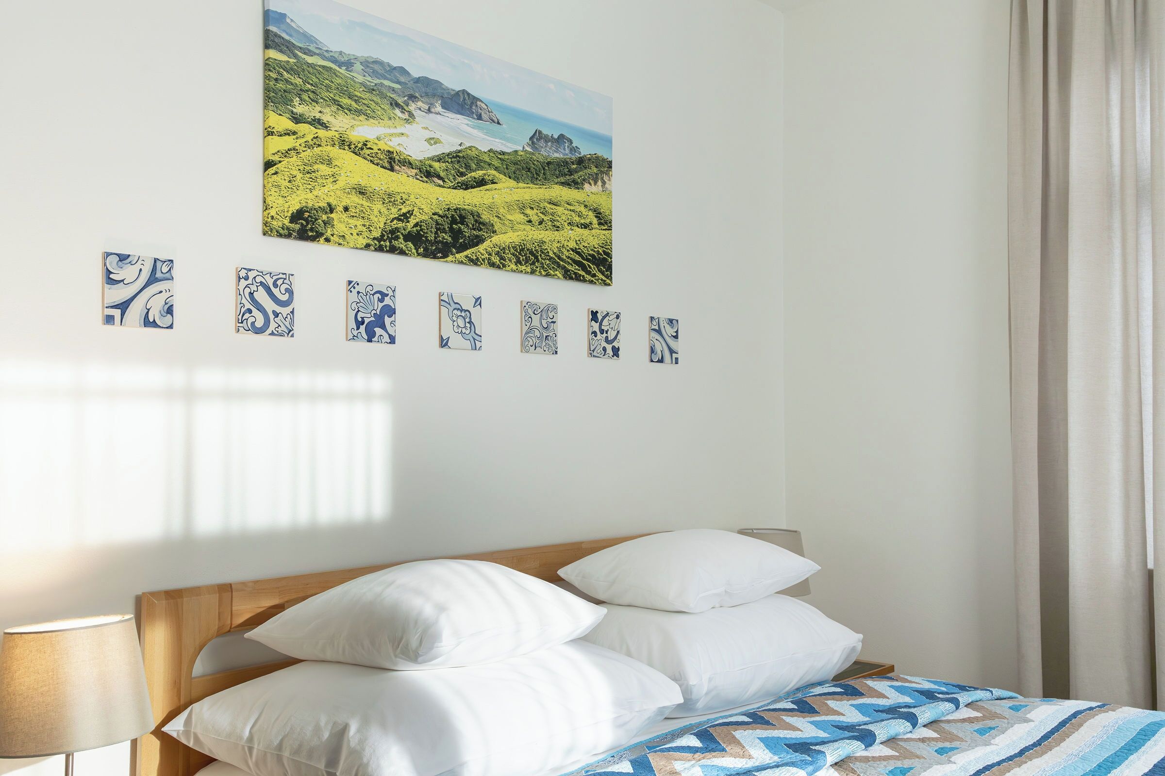 Une chambre à coucher avec un lit, des oreillers, une lampe, un tableau et une série de carreaux décoratifs sur le mur.