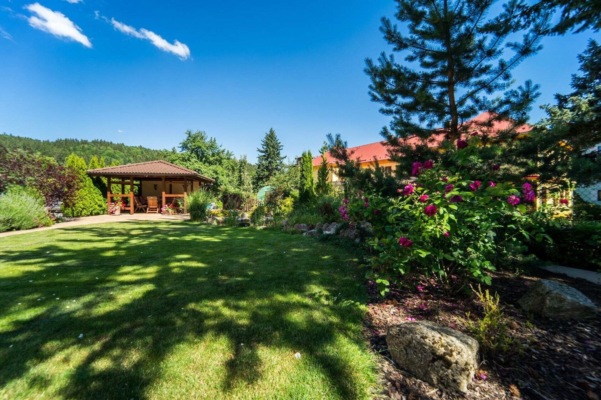 A house with a garden, a wooden gazebo, and a red-roofed building.