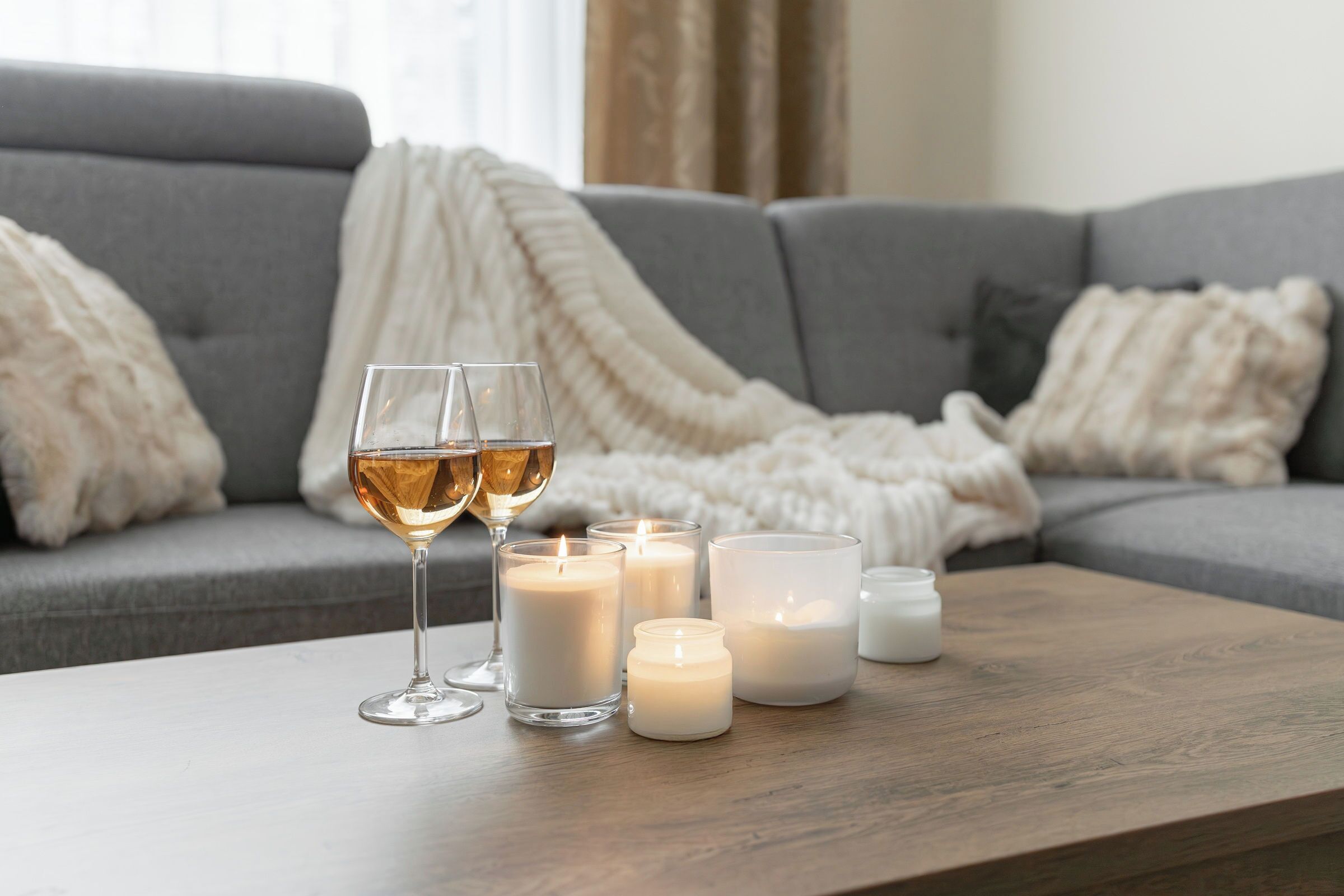A cozy living room with a grey sofa, a white throw blanket, and several lit candles on a wooden coffee table.