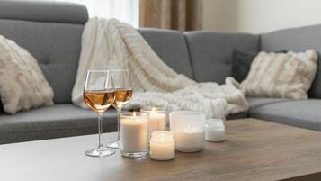 A cozy living room with a grey sofa, a white throw blanket, and several lit candles on a wooden coffee table.