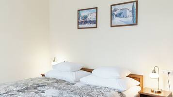 Una cama bien hecha con una colcha estampada, dos almohadas blancas, una mesita de noche con una lámpara y dos cuadros en la pared.