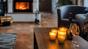 A cozy living room with a fireplace, candles, a bottle of wine, and a glass on a wooden table.