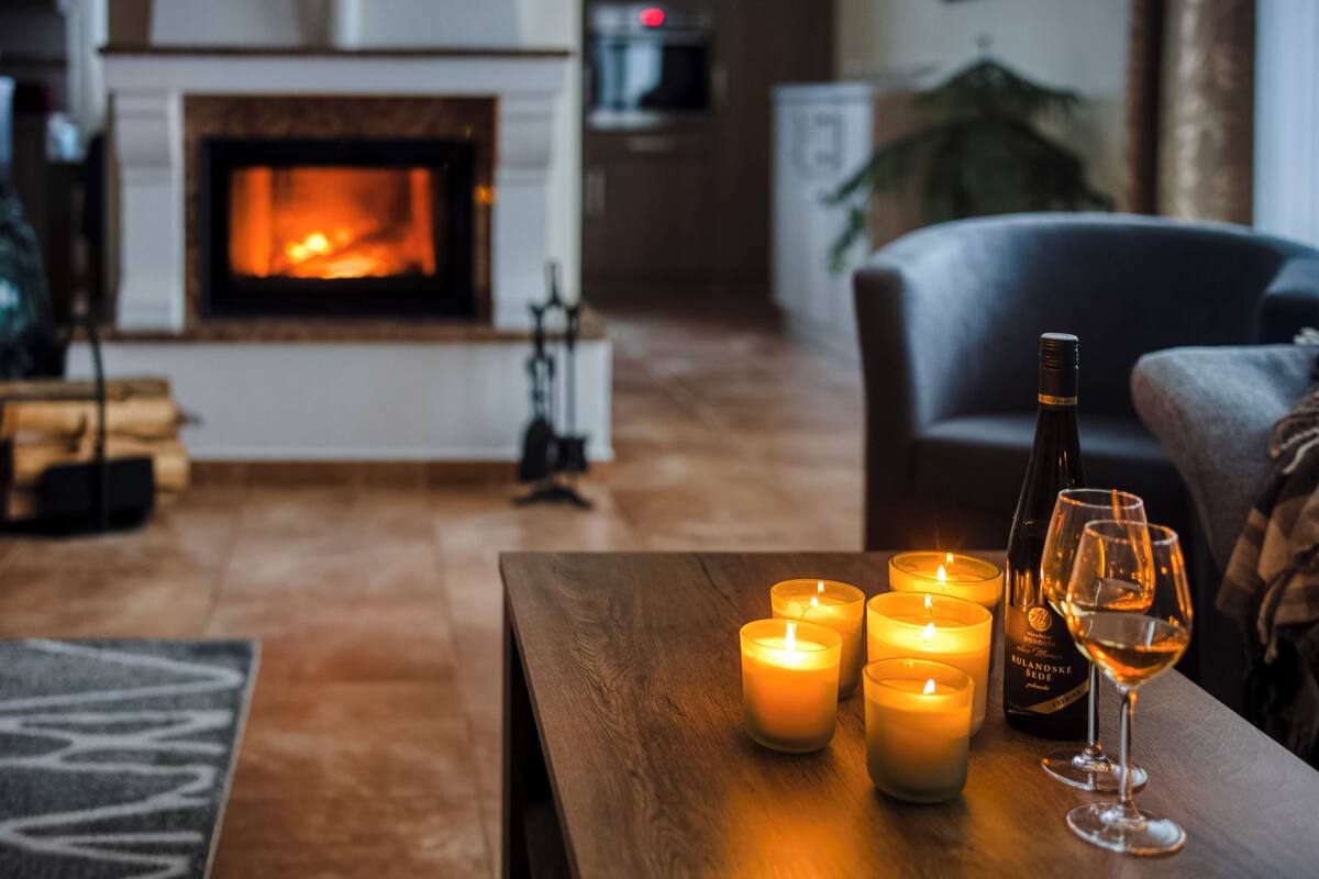 A cozy living room with a fireplace, candles, a bottle of wine, and a glass on a wooden table.