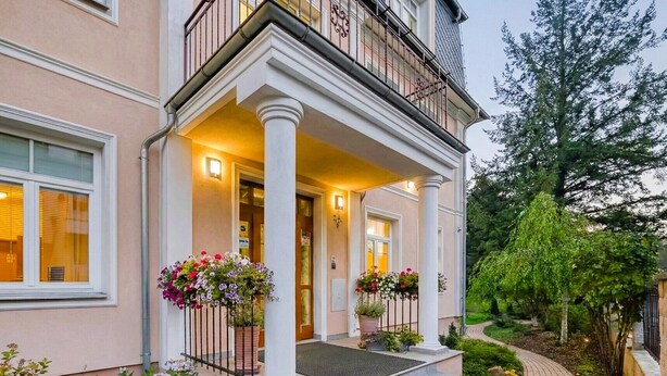 A two-story building with a covered porch, columns, and flower boxes.