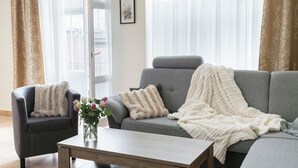 A living room with a grey sofa, a dark armchair, and a wooden coffee table. There is a vase with flowers on the coffee table.
