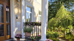 A building entrance with a covered porch, potted flowers, and a clear sky.