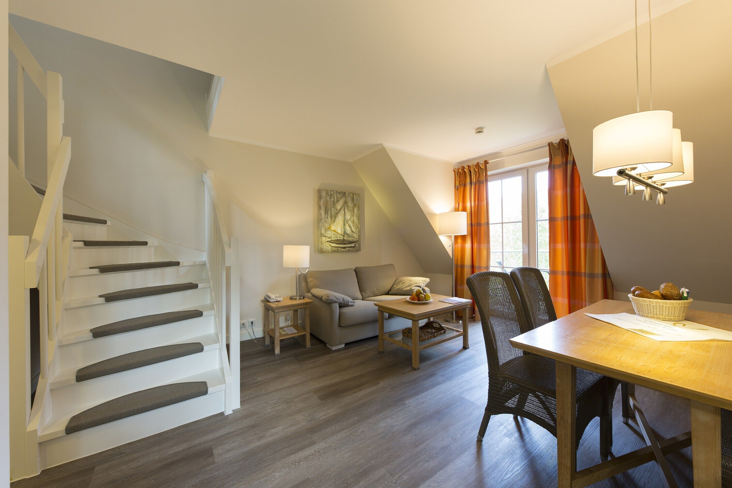 A modern loft-style room with a staircase, a sofa, a dining table, and a lamp.
