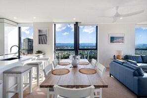 A modern living room with a dining area, large windows, and a city view. - 2 Bedroom Broadbeach Stay – Walk to Beach (Broadbeach)