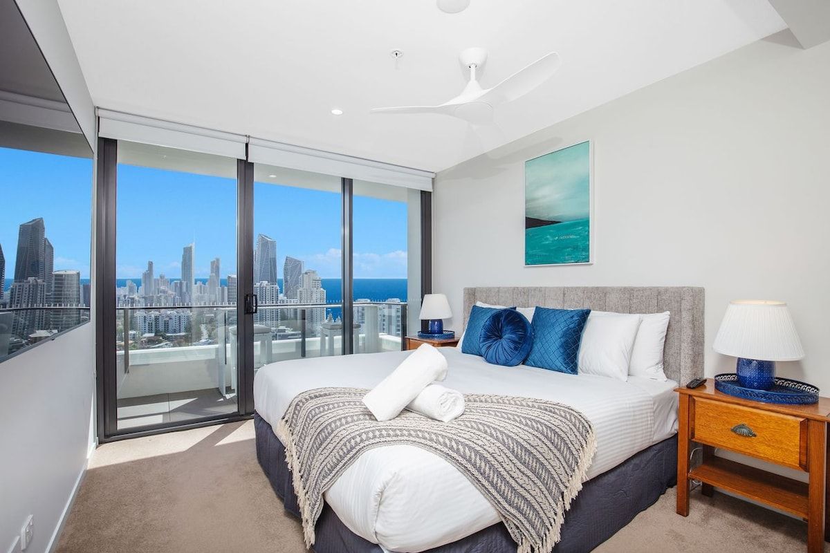 Un dormitorio moderno con una cama grande, un balcón con vistas a la ciudad y un ventilador de techo.
