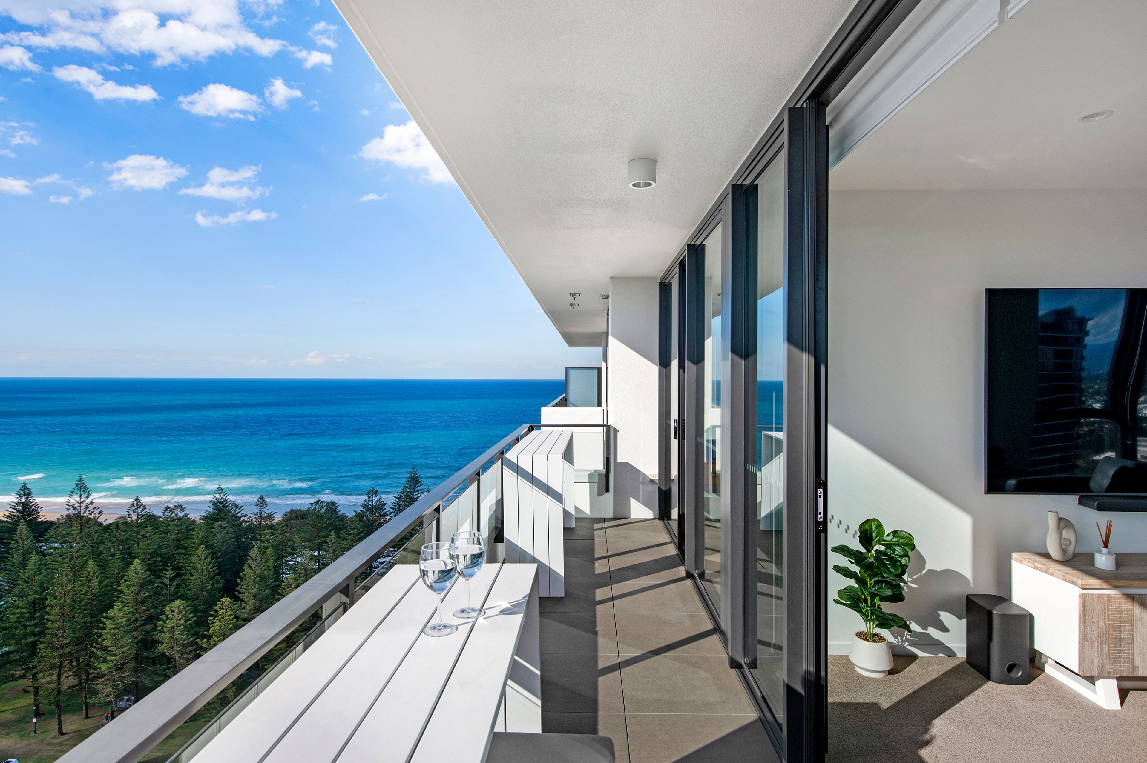 A balcony with a view of the ocean, a glass door, and a potted plant.