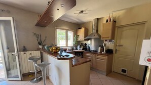 A kitchen with a central island, a stove, and a sink. There is a window with a view of greenery outside. - Villa Piscine 6 People (Corneilla-del-Vercol)