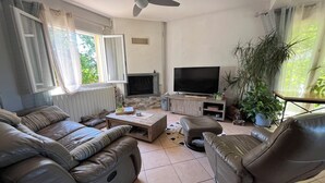 A living room with a sofa, armchair, coffee table, TV, fireplace, and potted plants. - Villa Piscine 6 People (Corneilla-del-Vercol)
