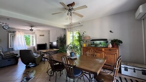 A dining area with a wooden table and chairs, a ceiling fan, a TV, and a potted plant. - Villa Piscine 6 People (Corneilla-del-Vercol)