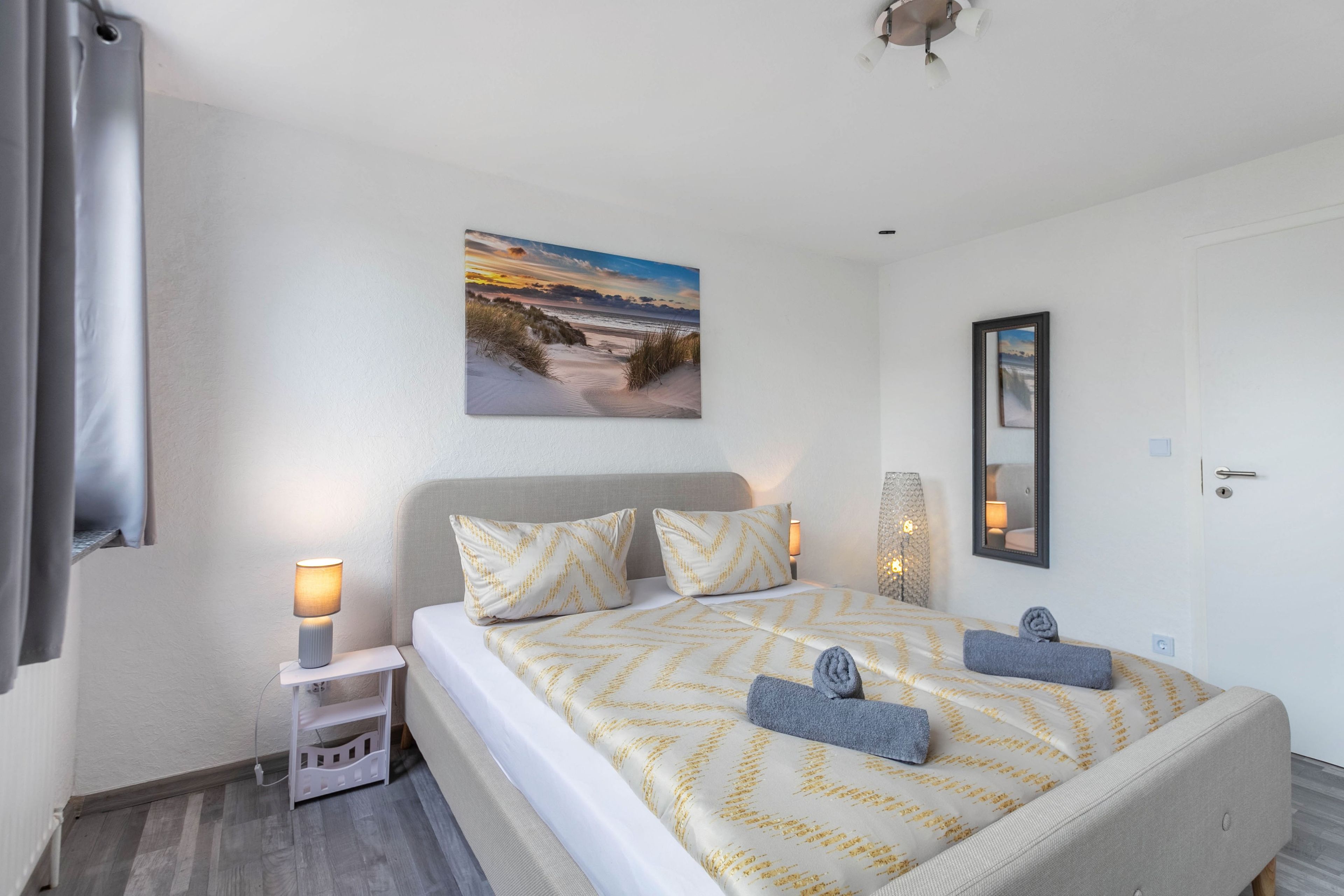 Ein Hotelzimmer mit einem Bett, zwei Nachttischlampen, einem Gemälde, einem Spiegel und einer Tür.