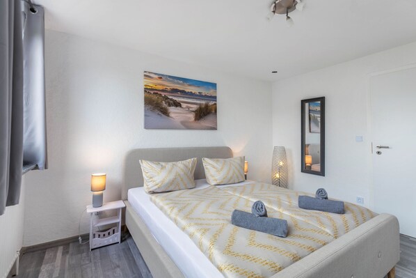 A hotel room with a bed, two bedside lamps, a painting, a mirror, and a door.