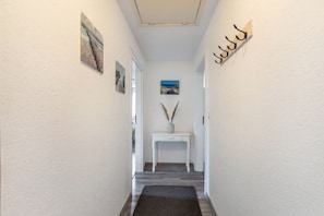 A hallway with a white door, a small white console table with a vase and pampas grass, and a wall-mounted coat rack.