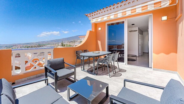 A balcony with a table and chairs, a view of the landscape, and a door leading to an interior space.