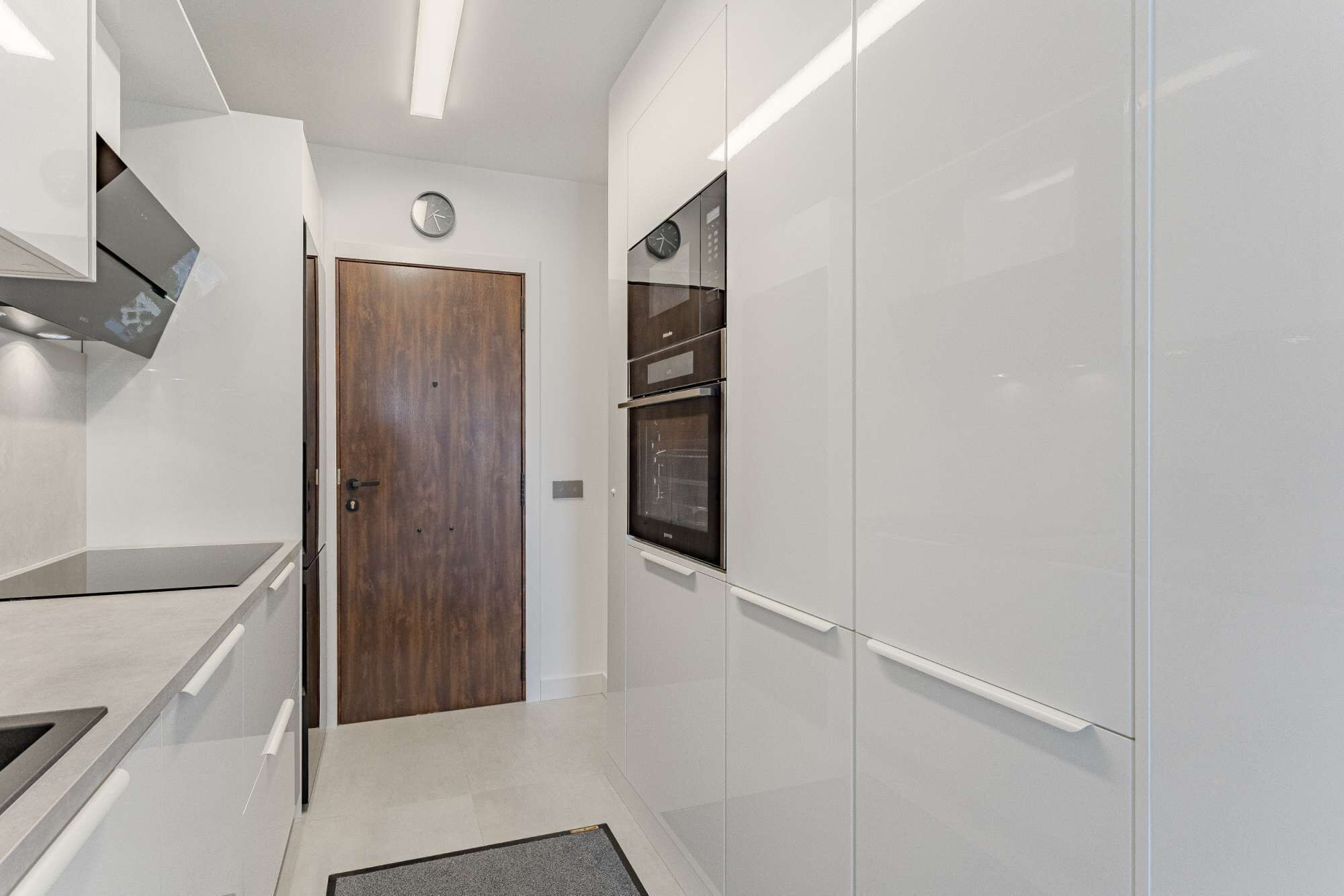 Una cocina moderna con armarios blancos, una puerta de madera y electrodomésticos integrados.