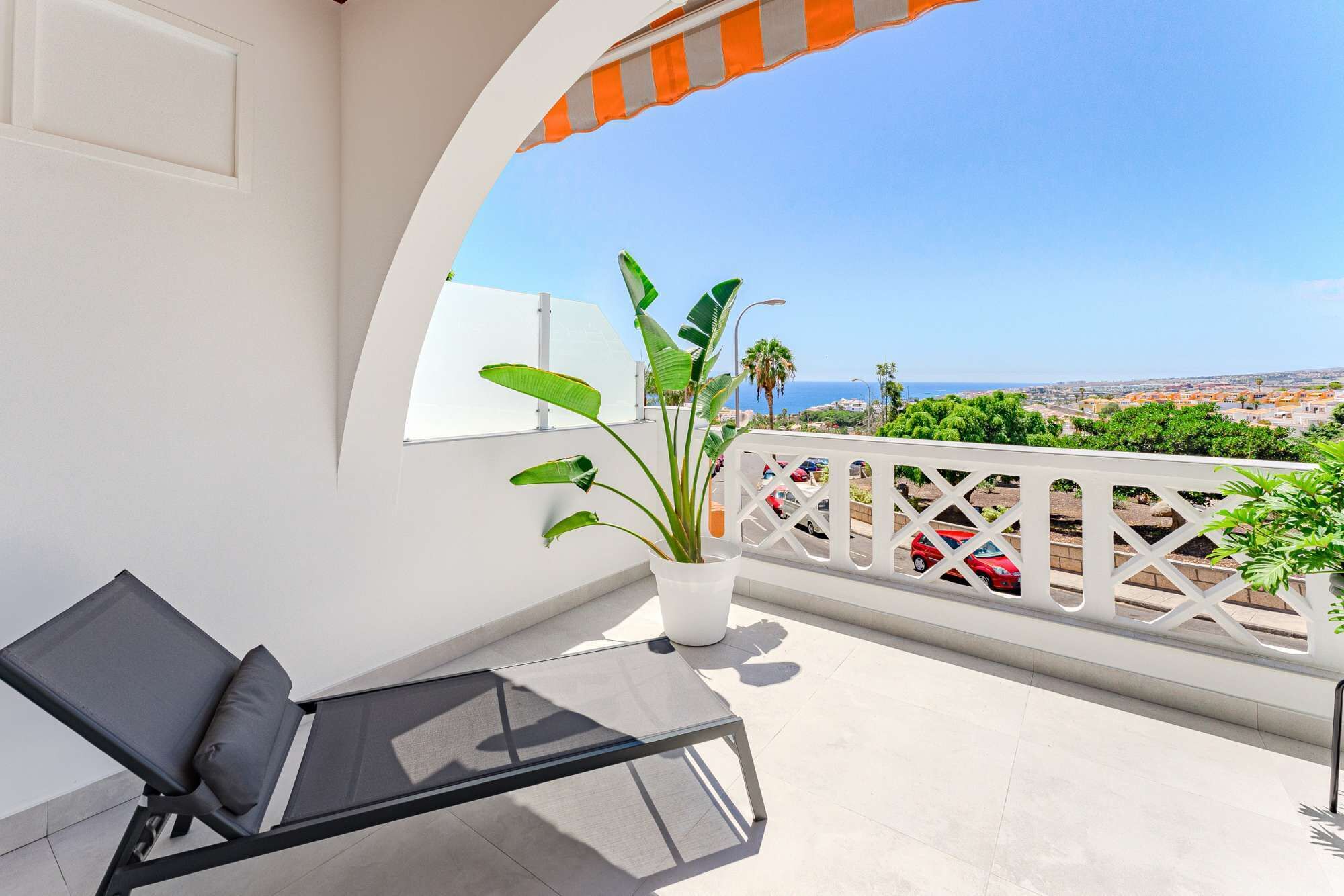 A balcony with a black lounge chair, a potted plant, and a view of the sea and cityscape.