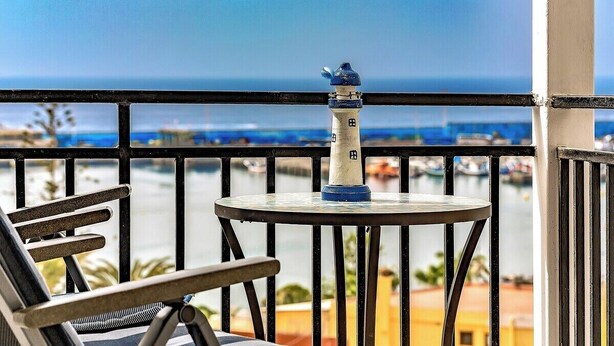 Un balcón con vista al mar, una mesita y una silla.