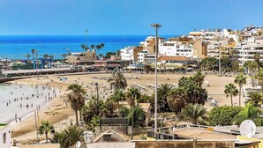 Un paisaje urbano costero con playa, palmeras y edificios.