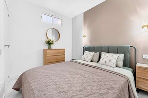 A bedroom with a bed, dresser, vanity, and a mirror.