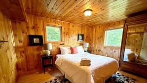 Une chambre à coucher aux murs lambrissés, comprenant un lit, deux tables de chevet, une fenêtre et un miroir.