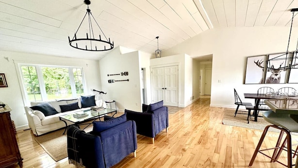 Un vaste salon doté d’un parquet, d’un canapé blanc, d’un canapé bleu, d’une table à manger avec des chaises et d’un lustre.
