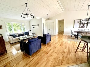 Un vaste salon doté d’un parquet, d’un canapé blanc, d’un canapé bleu, d’une table à manger avec des chaises et d’un lustre.