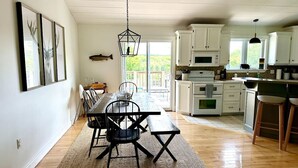 Une cuisine spacieuse avec des meubles blancs, une table à manger en bois et un luminaire suspendu.
