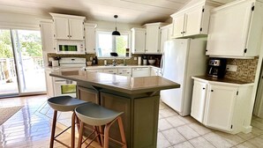 Une cuisine avec des meubles blancs, un grand îlot central doté de tabourets, un four à micro-ondes et un réfrigérateur.