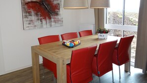 Un coin repas avec une table en bois, des chaises rouges, un tableau représentant un papillon et une fenêtre donnant sur un paysage.