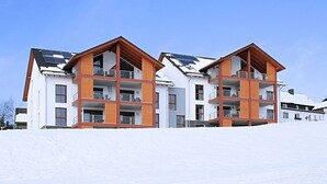 Un immeuble moderne à plusieurs étages, doté de balcons et de panneaux solaires, entouré de neige.