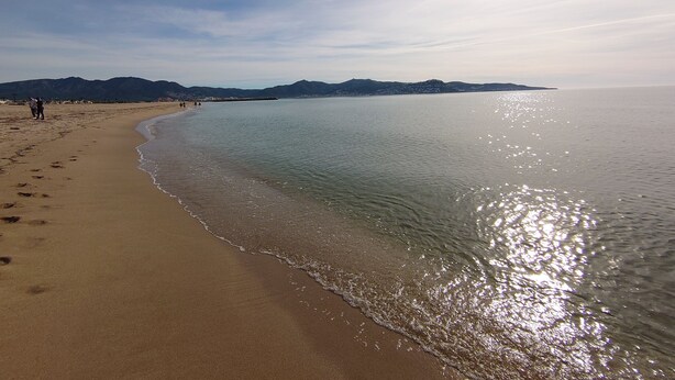 A beach with a clear sky, calm sea, and distant mountains. - Apt - Empuriabrava hyper center, beach and shops, view on natural park and sea (Empuriabrava)