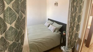 A bedroom with a bed, a nightstand, a wall-mounted lamp, and a curtain with a leaf pattern. - Apt - Empuriabrava hyper center, beach and shops, view on natural park and sea (Empuriabrava)
