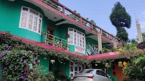 A two-story building with a balcony, a parked car, and various plants. - Bhagirath Homestay (Mirik)