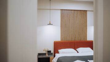A modern hotel room with a large bed, a bedside table with a vase of flowers, and a wooden slat wall panel.