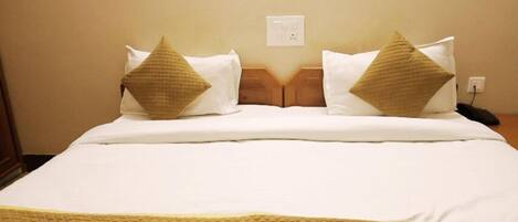 A neatly made bed with a white duvet and two beige pillows, a wooden headboard, and a power outlet on the wall.
