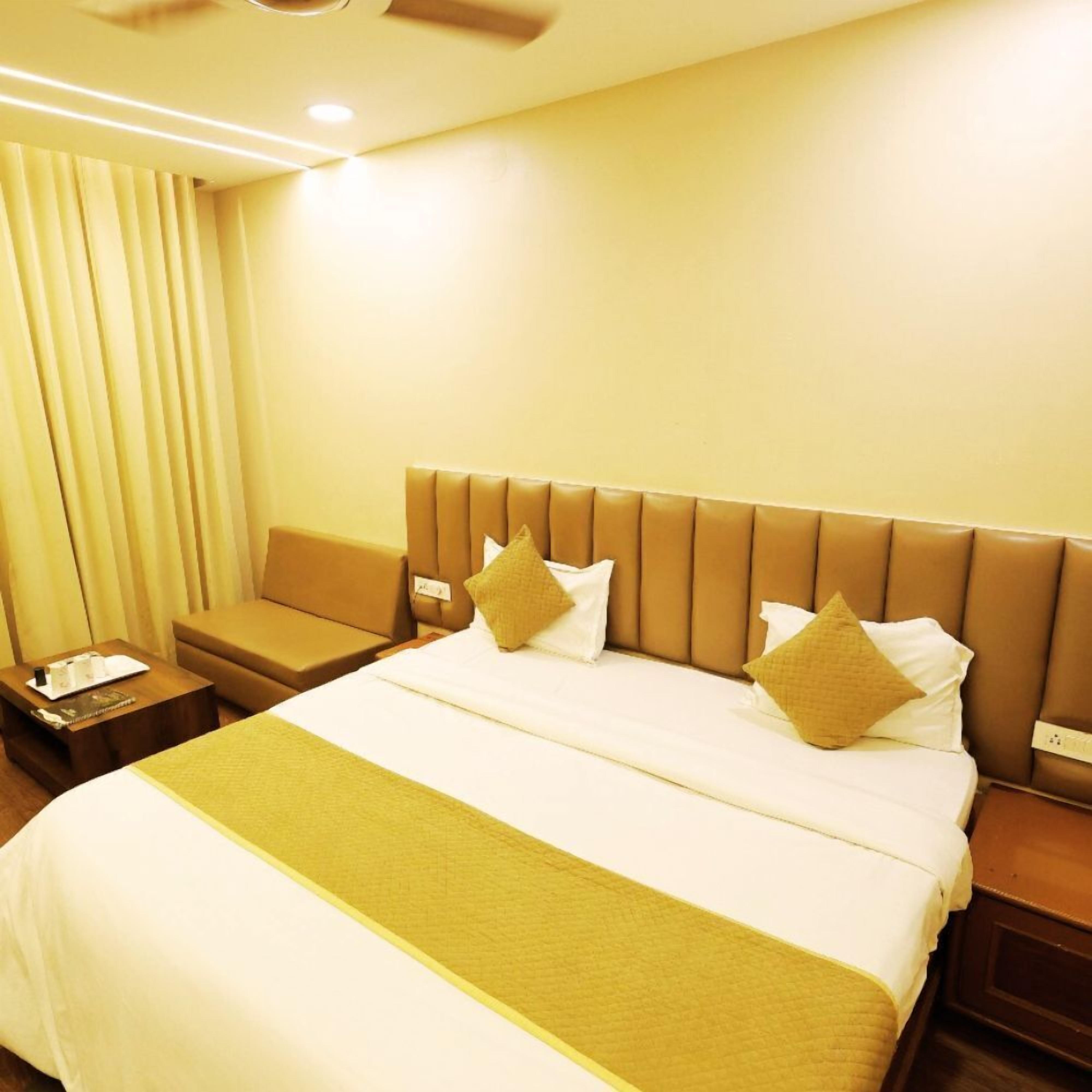 Quarto de hotel com uma cama grande, uma mesa de cabeceira, um sofá e uma janela com cortinas.