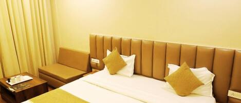 Quarto de hotel com uma cama grande, uma mesa de cabeceira, um sofá e uma janela com cortinas.