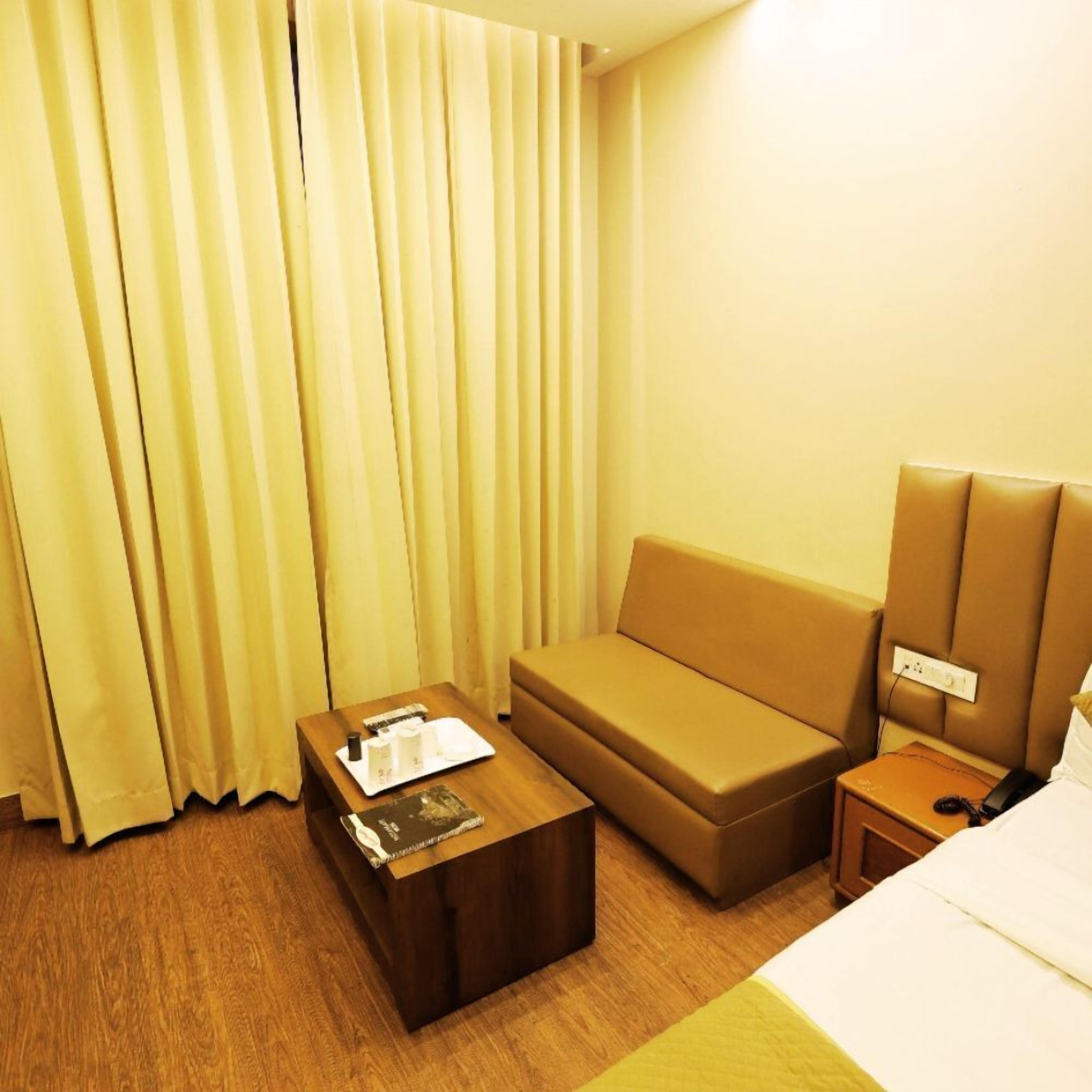 Una camera d'albergo con un letto, un divano marrone, un tavolino in legno e un comodino con una lampada.
