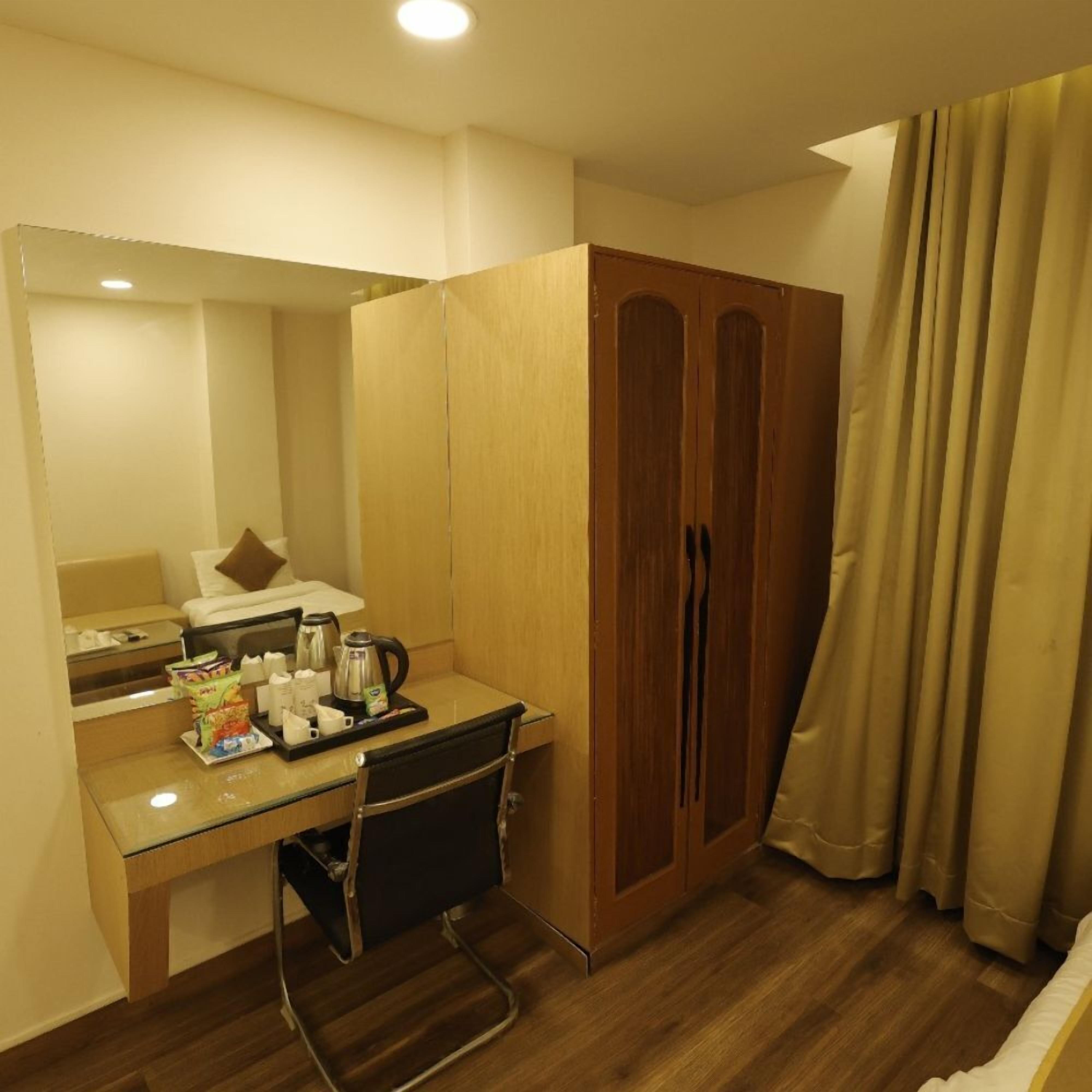 A hotel room with a wooden desk, a chair, a wardrobe, and a bed.