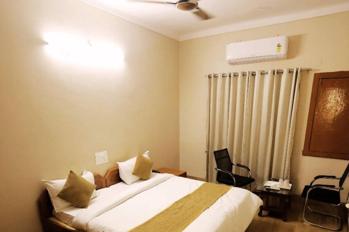 Hotellihuone, jossa on suuri sänky, työpöytä, tuoli, ilmastointilaite ja ikkuna, jossa on verhot.
