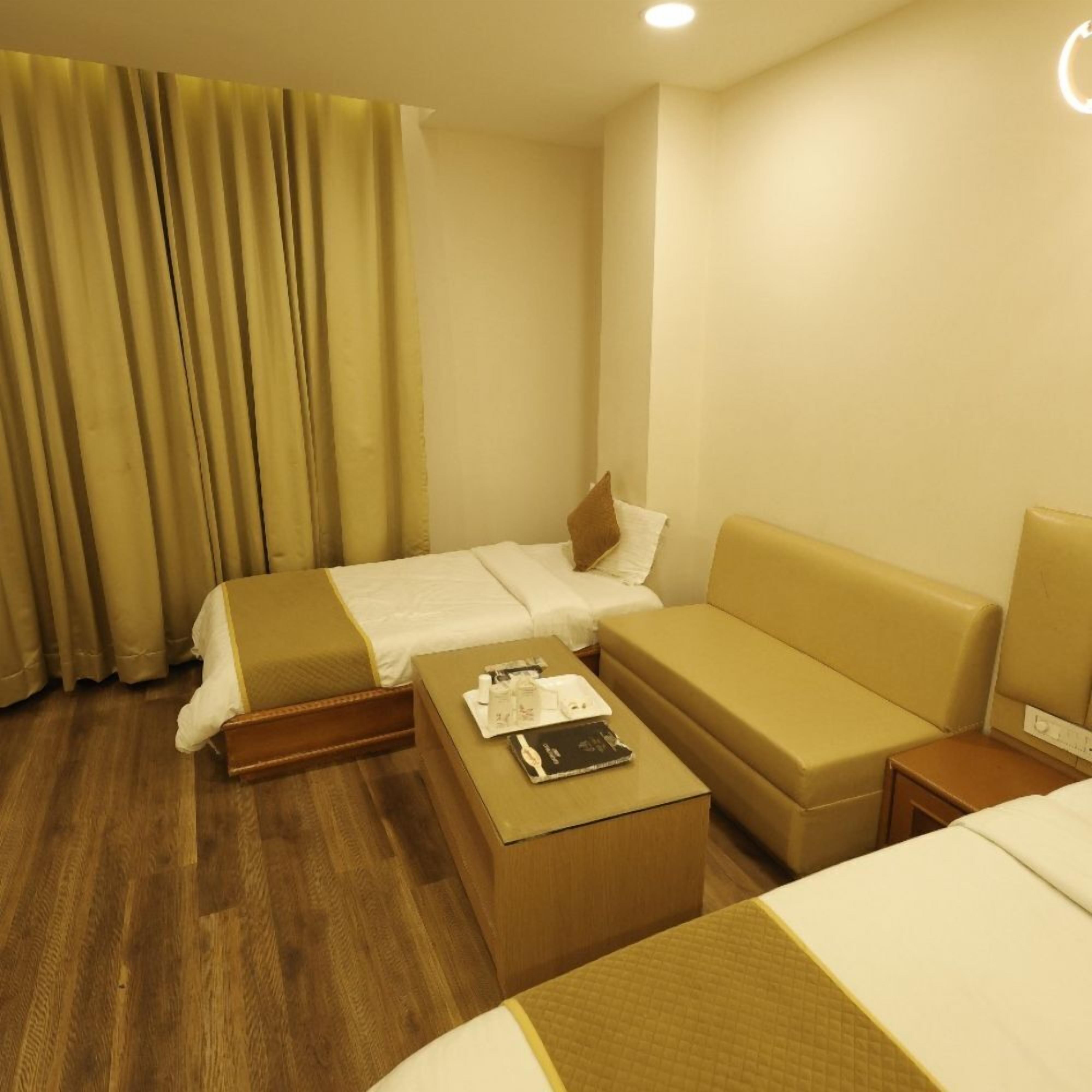 A hotel room with two beds, a sofa, a coffee table, and a lamp.