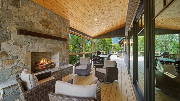 A covered outdoor area with wicker furniture, a stone fireplace, and a view of the outdoors.