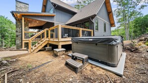 A modern house with a stone chimney, a wooden deck, and a hot tub.