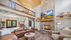 A spacious living room with a leather sofa, a round coffee table, and a stone fireplace.