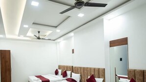 A hotel room with four beds, marble flooring, ceiling fans, and a large mirror. - The Satnam Inn (Varanasi)