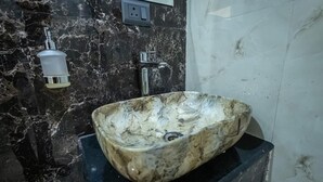 A bathroom with a marble sink, a soap dispenser, and a faucet. - The Satnam Inn (Varanasi)
