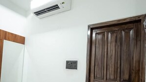 A room with a wooden door, a white wall, a marble-patterned floor, and a ceiling-mounted air conditioner. - The Satnam Inn (Varanasi)